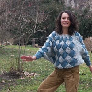 May include: A woman wearing a blue and gray patterned sweater with a diamond design. She is wearing brown corduroy pants and is smiling at the camera.