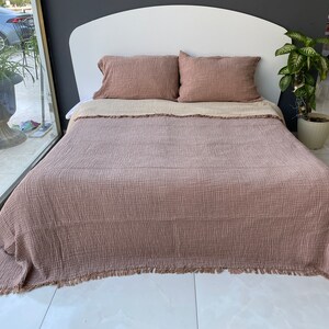 Puede incluir: Una manta de tejido de gofre marrón con flecos en un marco de cama blanco con dos almohadas marrones. La manta está doblada hacia atrás para mostrar la ropa de cama blanca debajo.
