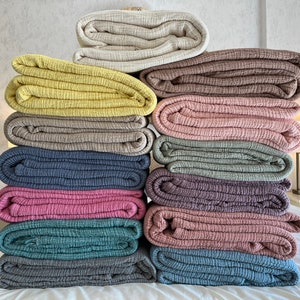 K&ouml;nnte beinhalten: Ein Stapel von 12 gefalteten Waffelgewebe-Baumwolldecken in verschiedenen Farben, darunter Beige, Gelb, Braun, Rosa, Blau und Grau.