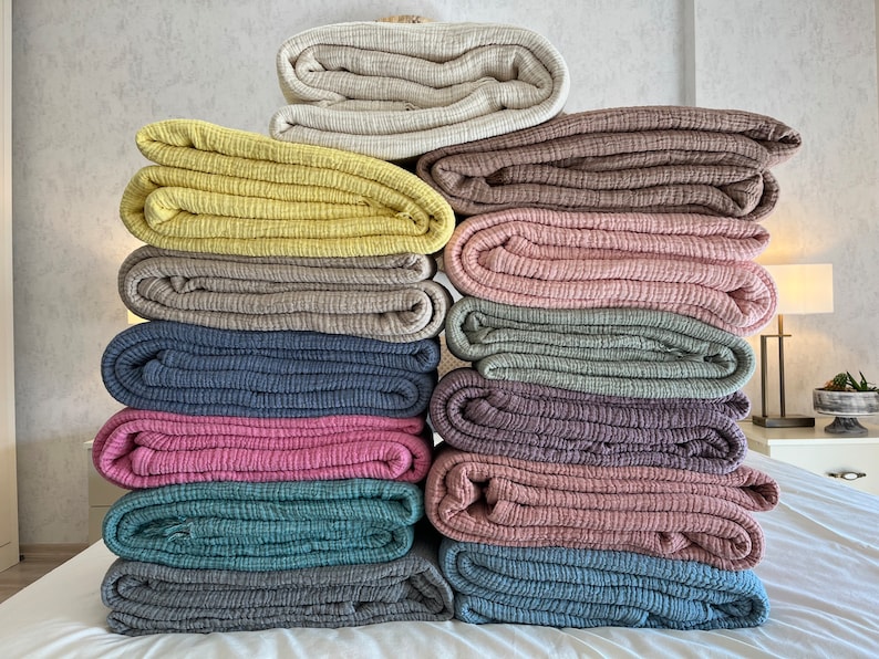 K&ouml;nnte beinhalten: Ein Stapel von 12 gefalteten Waffelgewebe-Baumwolldecken in verschiedenen Farben, darunter Beige, Gelb, Braun, Rosa, Blau und Grau.