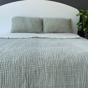 May include: A bed with a white headboard, covered with a light green textured bedspread and two matching pillows. The bedspread and pillows have a crinkled appearance, suggesting a soft, breathable fabric. The overall aesthetic is simple and calming.