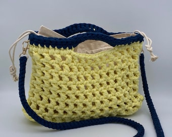 May include: A yellow crocheted bag with a navy blue trim and a long navy blue strap. The bag has a woven design and is made of cotton.