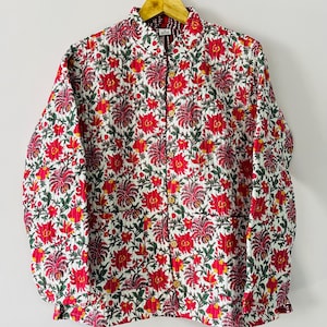 May include: A long-sleeve quilted jacket featuring a white base with a dense floral pattern in shades of red, pink, and green. The jacket has a collared neckline, a front button closure with light brown buttons, and two front pockets.