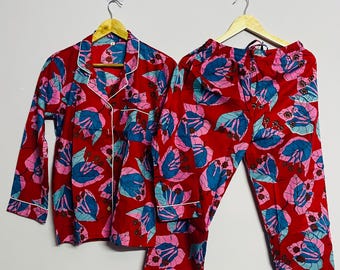 Puede incluir: Conjunto de pijama rojo con estampado floral en rosa y azul. La parte superior de manga larga y los pantalones tienen ribetes blancos. Los pijamas están colgados en perchas de madera.