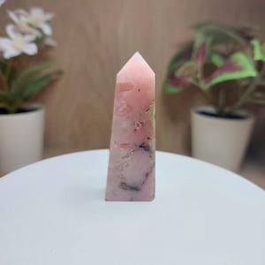 May include: A pink and white crystal point with a pointed tip and a smooth, polished surface.