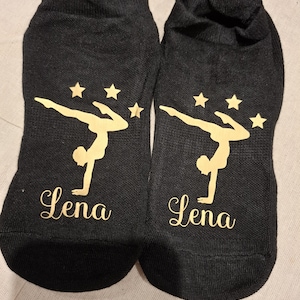 May include: A pair of black ankle socks featuring a gold gymnast silhouette and five gold stars. The socks are personalised with the name "Lena" on each sock.