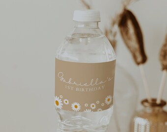 May include: A clear plastic water bottle with a brown label that says "Gabriella's 1st Birthday" with white daisies and yellow centers. The bottle is on a wooden coaster.