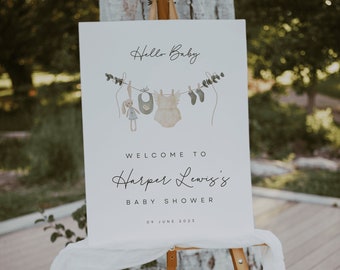 May include: A white sign with a welcome to Harper Lewis's baby shower announcement. The sign has a watercolour illustration of baby clothes hanging on a clothesline with a cute bunny doll.