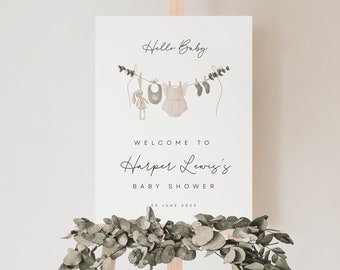 May include: A white welcome sign with the text "Hello Baby" and a line of baby clothes hanging on a clothesline. The text "Welcome to Harper Lewis's Baby Shower" is below the clothesline. The date "09 June 2023" is at the bottom of the sign.