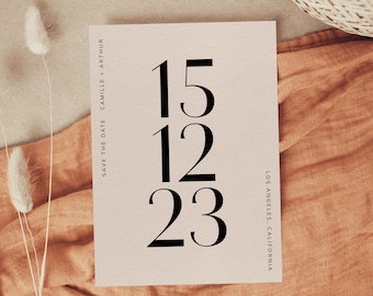 以下が含まれることがあります： クリーム色の背景に黒で「15.12.23」と日付が書かれたシンプルな結婚式の招待状。カードの右側に黒で「Save the Date Camille + Arthur」と印刷されています。カードの左側に黒で「ロサンゼルス、カリフォルニア」と印刷されています。