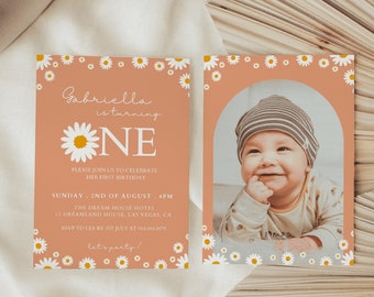Peut inclure: Une invitation de premier anniversaire de couleur pêche avec une bordure de marguerites blanches. L'invitation présente une grande marguerite blanche avec un centre jaune et le texte "Gabriella a un an". L'invitation comprend également la date, l'heure et le lieu de la fête. Une carte séparée avec un fond pêche et une bordure de marguerites blanches présente une photo d'une petite fille portant un chapeau rayé.