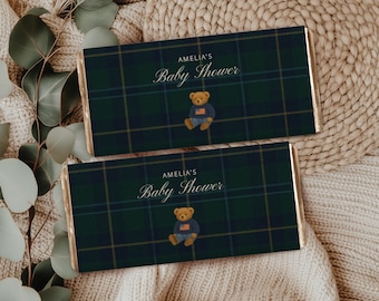 Op de afbeelding: Twee chocoladereepverpakkingen met een groen en marineblauw ruitpatroon. De verpakkingen hebben de tekst "AMELIA'S Baby Shower" en een teddybeer-afbeelding in een blauwe trui en jeans. Op een beige oppervlak.