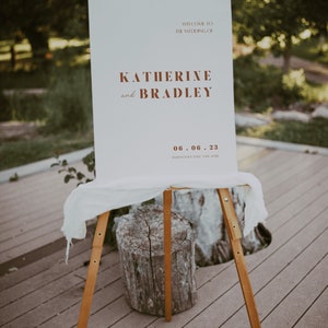 May include: White wedding sign with brown text announcing the wedding of Katherine and Bradley on 06.06.23. The sign is on an easel.