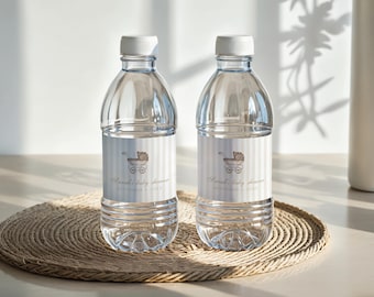 Könnte beinhalten: Zwei transparente Plastikwasserflaschen mit weißen Deckeln, jeweils mit einem Etikett mit der Aufschrift "Sweet Baby Shower" und einer Kinderwagenillustration. Die Flaschen stehen auf einem gewebten Platzset.