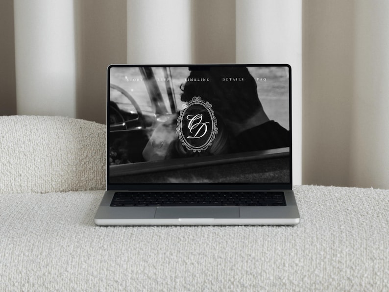 May include: A laptop displaying a website with a black and white image of a person in a car. The website's logo is a monogram within a decorative frame. The laptop is on a white textured surface.