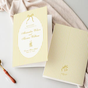 Peut inclure: Deux cartons d'invitation de mariage crème à rayures verticales. L'un est ouvert, affichant du texte dans un ovale, et l'autre est fermé. Un nœud doré et du texte sont sur le devant. Un sceau de cire doré et une cuillère sont sur le côté.