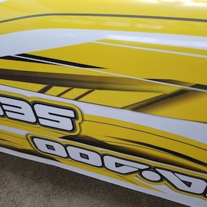 May include: Close-up of a yellow and white graphic design with the word "Sea-Doo" in black and white lettering.