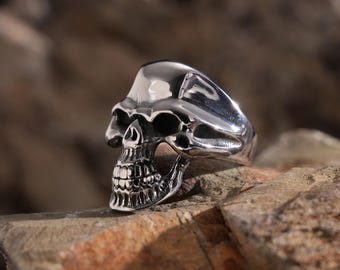 May include: A silver skull ring with a detailed design. The ring is made of stainless steel and has a polished finish.
