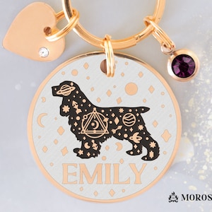 May include: A gold-tone dog tag with a black silhouette of a cocker spaniel with a celestial design. The tag has the name "EMILY" engraved on it.