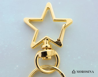 Puede incluir: Llavero de estrella dorado con cierre giratorio y un anillo. El llavero está sobre un fondo blanco.
