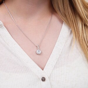 Peut inclure: Un collier en chaîne argent avec un pendentif rond orné d'une grosse pierre de zircone cubique transparente entourée de plus petites pierres de zircone cubique.