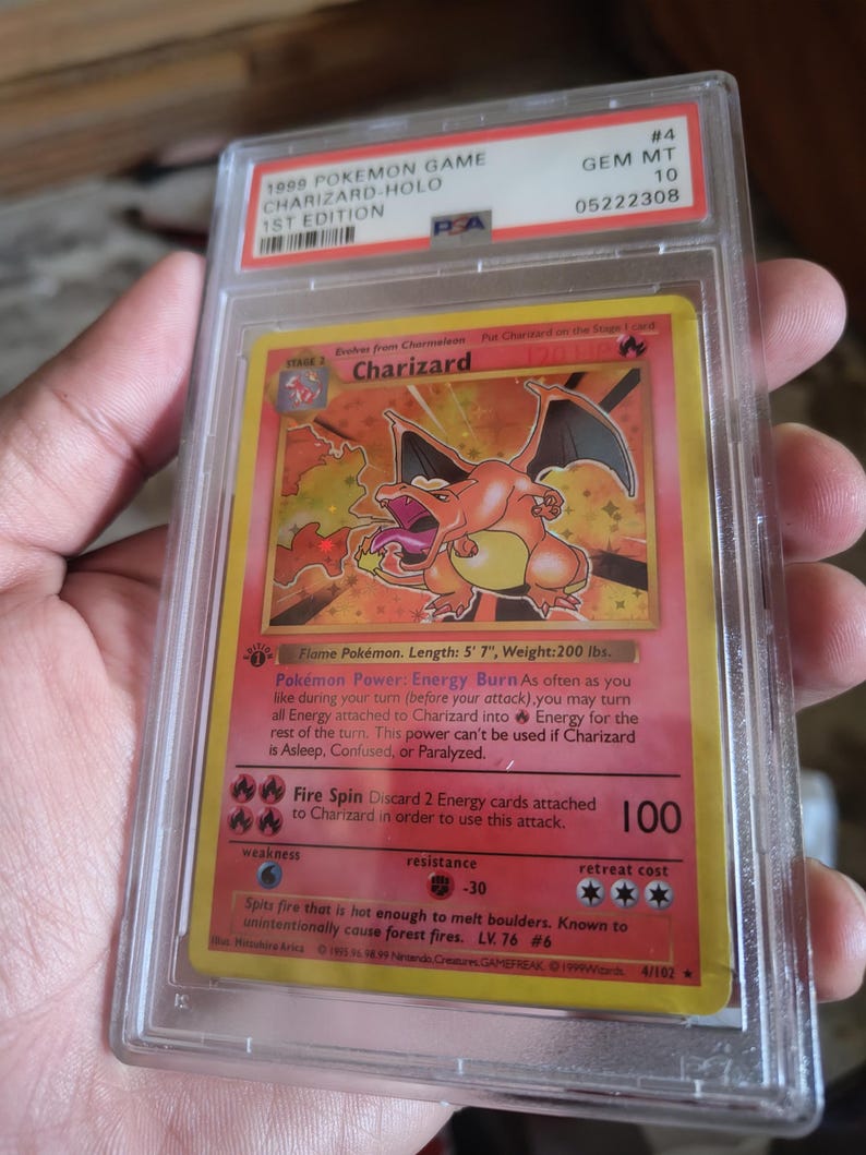 K&ouml;nnte beinhalten: Eine bewertete 1999 Pok&eacute;mon Game Charizard Holo 1st Edition Karte. Die Karte zeigt eine Charizard-Illustration mit einem rot-orangen Farbschema. Die Karte ist in einem Schutzhalter mit einer PSA-Note von 10 eingeschlossen.