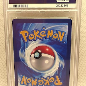 K&ouml;nnte beinhalten: Eine bewertete Pok&eacute;mon-Sammelkarte in einem transparenten Kunststoffhalter. Die Karte zeigt das Pok&eacute;mon-Logo und ein Pok&eacute;ball-Design auf blauem Hintergrund. Der Halter hat ein PSA-Etikett mit einer Seriennummer.