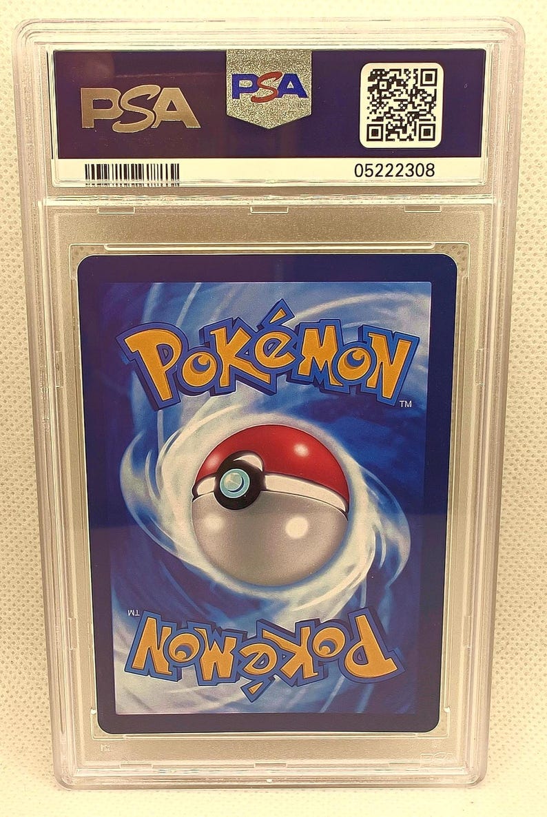 K&ouml;nnte beinhalten: Eine bewertete Pok&eacute;mon-Sammelkarte in einem transparenten Kunststoffhalter. Die Karte zeigt das Pok&eacute;mon-Logo und ein Pok&eacute;ball-Design auf blauem Hintergrund. Der Halter hat ein PSA-Etikett mit einer Seriennummer.