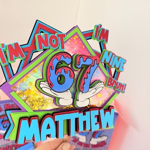 Puede incluir: Adorno de pastel de cumpleaños colorido con el texto "I'm not nine, I'm 67, bruh!" y el nombre "Matthew". El diseño presenta elementos en capas azules, rojos, verdes y morados, con manos de dibujos animados sosteniendo el número 67.