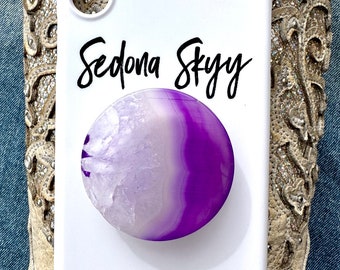 May include: White phone case with a purple and white agate stone pop socket. The case has the text "Sedona Skyy" and "@SedonaSkyyGems" printed on it.