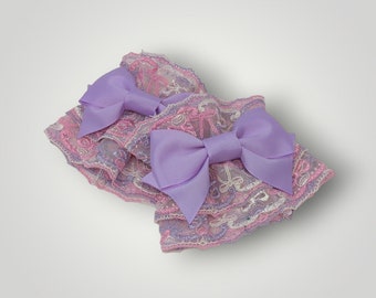 May include: Two purple satin bows with pink and white lace trim. The bows are layered on top of each other.