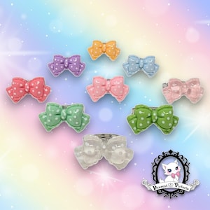 May include: A collection of ten bow-shaped rings in various colors including orange, purple, blue, pink, green, and clear, each featuring a white polka dot pattern. A logo in the bottom right corner displays a white cat and the text Dearest Victoria.