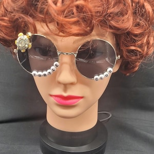 May include: Round silver sunglasses with black lenses and white beads spelling "TURTLE CLUB" on the frames. A small turtle charm is attached to the left frame.