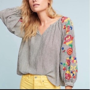 May include: A striped blouse with a V-neck and floral embroidery on the sleeves. The blouse has vertical grey and white stripes, and the embroidery features red, yellow, and blue flowers. The sleeves are long.