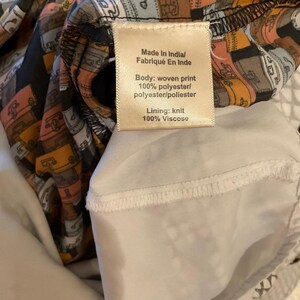 Puede incluir: Primer plano de una etiqueta de prenda con texto. La etiqueta dice "Made In India/Fabriqu&eacute; En Inde". El cuerpo es de tejido estampado, 100% poli&eacute;ster. El forro es de punto, 100% viscosa. La prenda tiene un estampado de maletas.