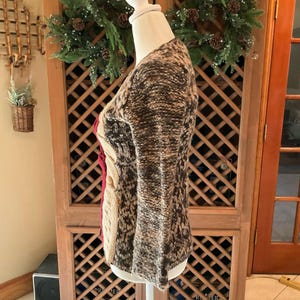 May include: A multi-colored sweater with a cable knit design. The sweater features a mix of brown, beige, and red hues. The sleeves are long and flared. The sweater is displayed on a mannequin.
