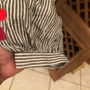May include: Close-up of a striped sleeve with floral embroidery. The sleeve is black and white striped with a gathered cuff. The embroidery features red and pink flowers.