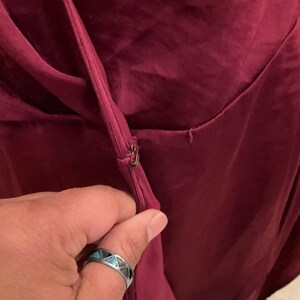 Puede incluir: Primer plano de un vestido burdeos con cremallera dorada. La tela parece ser un material liso y fluido. El vestido es de color rojo-p&uacute;rpura oscuro.