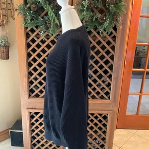 Pode incluir: Um su&eacute;ter preto de malha canelada exposto em um manequim. O su&eacute;ter tem gola redonda e mangas compridas. O tecido tem canelado vertical. O su&eacute;ter &eacute; de cor s&oacute;lida e parece ser feito de um material macio. O su&eacute;ter &eacute; um estilo cl&aacute;ssico.