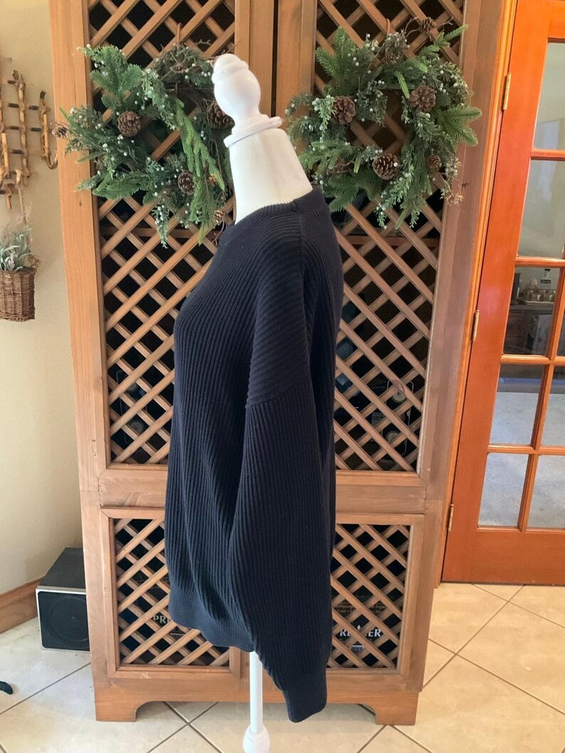 Pode incluir: Um su&eacute;ter preto de malha canelada exposto em um manequim. O su&eacute;ter tem gola redonda e mangas compridas. O tecido tem canelado vertical. O su&eacute;ter &eacute; de cor s&oacute;lida e parece ser feito de um material macio. O su&eacute;ter &eacute; um estilo cl&aacute;ssico.