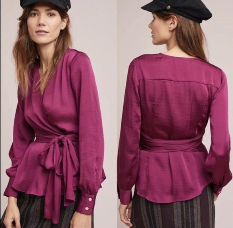 Puede incluir: Top envolvente de manga larga en color magenta intenso. Presenta un escote en V, cierre de lazo en la cintura y pu&ntilde;os abotonados. La tela tiene un brillo sutil, sugiriendo sat&eacute;n o seda. El dise&ntilde;o es elegante y femenino, ideal para ocasiones especiales.