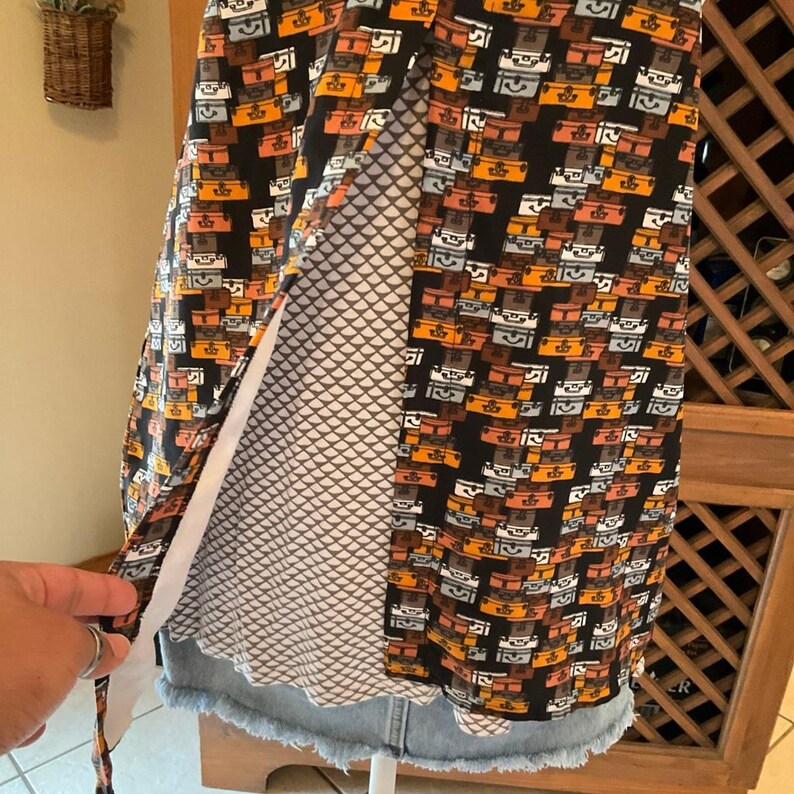 Puede incluir: Vestido negro y naranja estampado con dise&ntilde;o de maletas. El vestido tiene un dobladillo de mezclilla y un forro estampado en blanco y gris. El vestido es sin mangas y parece estar hecho de una tela ligera.