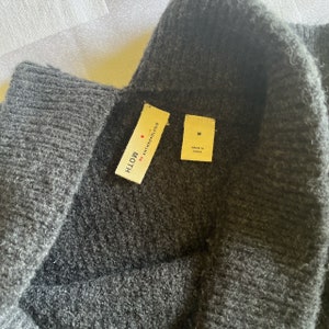 May include: A dark gray sweater with a black turtleneck collar. The sweater has a tag that reads "MOTH by ANTHROPOLOGIE" and another tag that reads "M MADE IN CHINA".