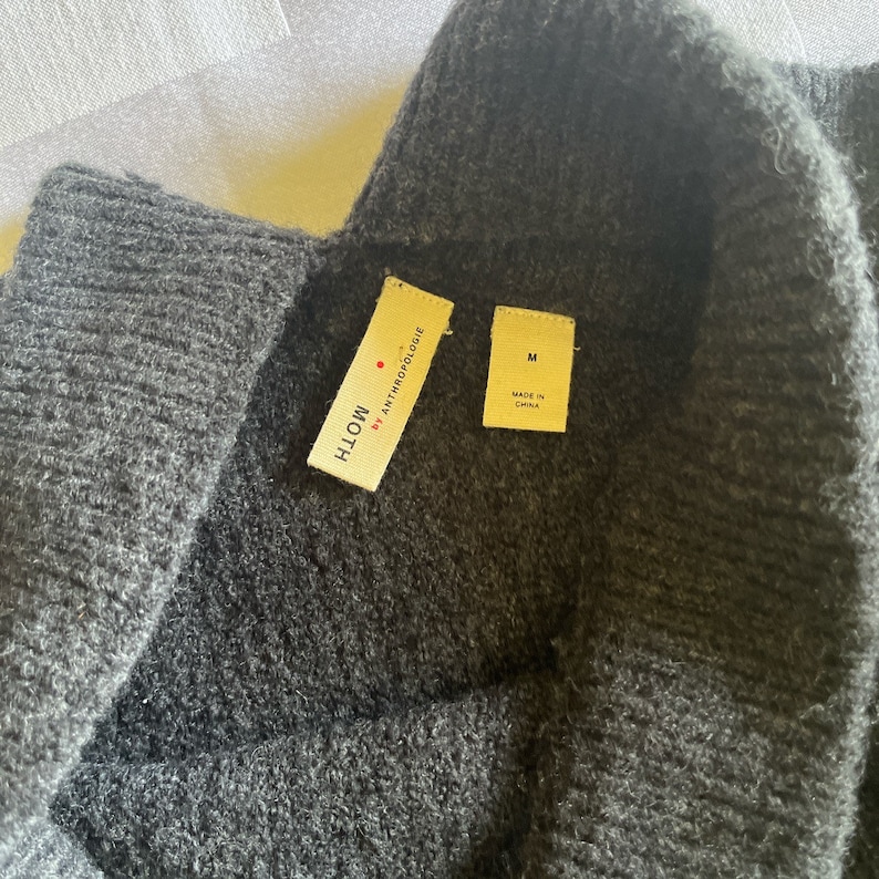 May include: A dark gray sweater with a black turtleneck collar. The sweater has a tag that reads "MOTH by ANTHROPOLOGIE" and another tag that reads "M MADE IN CHINA".