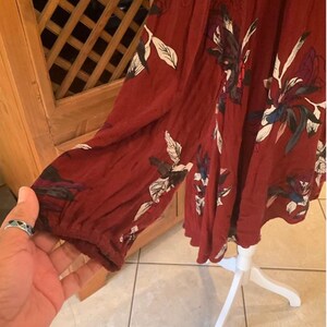 May include: A burgundy-colored dress with long sleeves and a floral pattern in white, black, and blue. The dress has a lace detail at the neckline and is displayed on a white dress form.