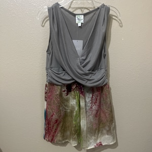 Pode incluir: Um top cinza sem mangas com um detalhe cruzado no busto, sobreposto a uma saia transparente com estampa floral. A saia tem uma base branca com estampas florais rosa, verde e marrom.