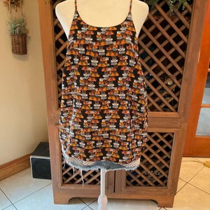 Puede incluir: Un top de camisola negro con un patr&oacute;n repetido de rect&aacute;ngulos naranjas, marrones y blancos. El top tiene finas correas de espagueti y un escote redondo. El dobladillo inferior est&aacute; deshilachado y parece ser de mezclilla. El top se muestra en un maniqu&iacute;.