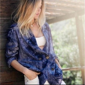 May include: A blue tie-dye blazer with large brown buttons. The blazer has a double-breasted design and is paired with white shorts. The jacket's pattern is a mix of dark and light blue hues.