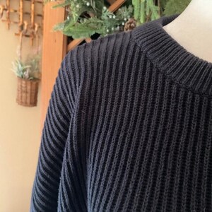 Pode incluir: Uma caneca de cer&acirc;mica branca com uma al&ccedil;a preta e o texto "But First, Coffee" em negrito preto. A caneca est&aacute; sobre um fundo desfocado, sugerindo um ambiente acolhedor.