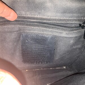 May include: Interior view of a black fabric bag with a zipper and a leather tag. The tag has text and the number 1953390. The bag's interior is dark and textured.